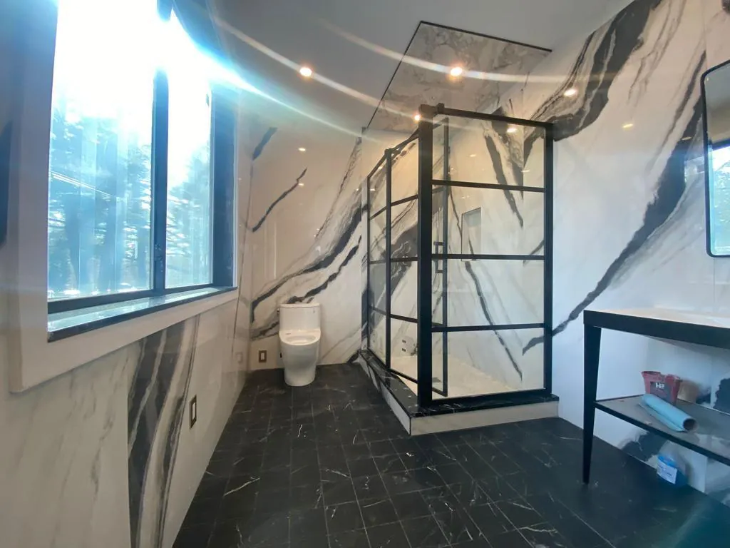Bathroom with bold veined marble-style walls and a black-framed glass shower