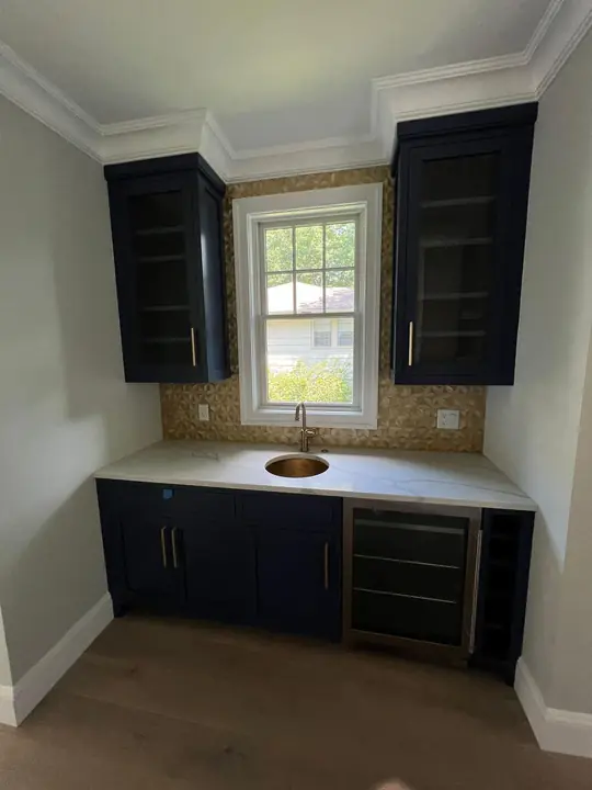 Wet bar with a tile backsplash between navy cabinets