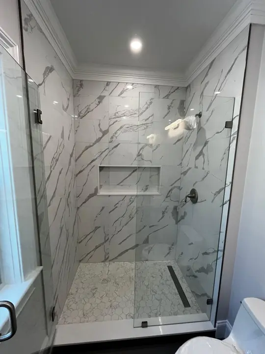 Walk-in glass shower with marble-style walls, niche and linear drain