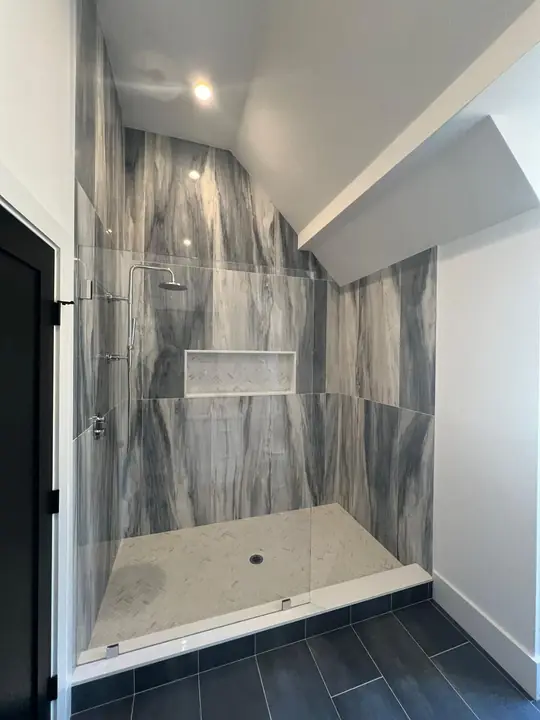 Shower with gray veined wall tile and a niche, over a dark plank floor