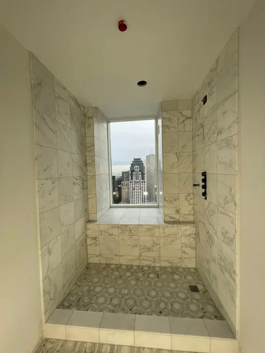 Shower with marble-style walls, a window and mosaic floor